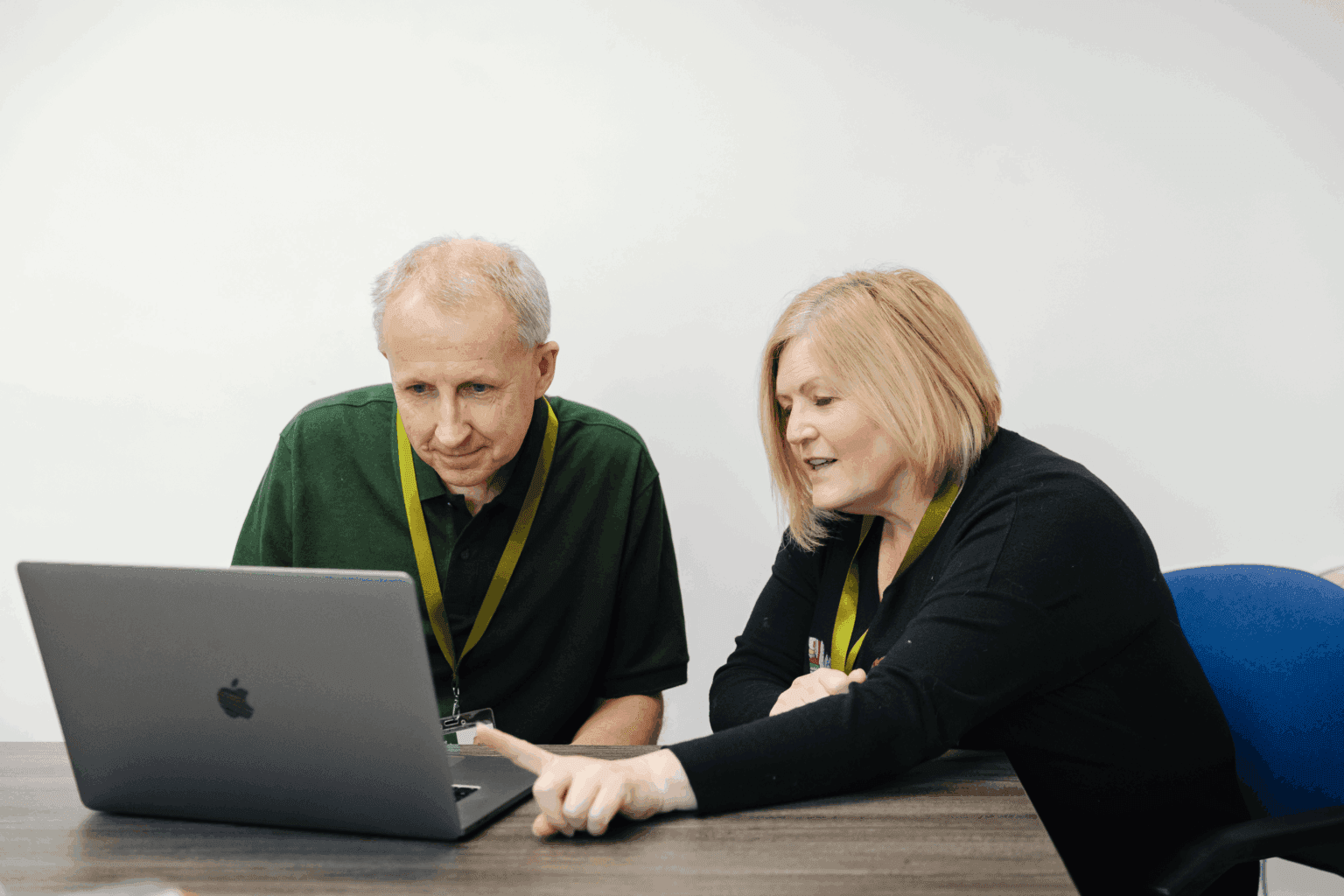 Two colleagues sitting at a desk looking at a laptop screen, with one pointing at the screen. - Home Instead