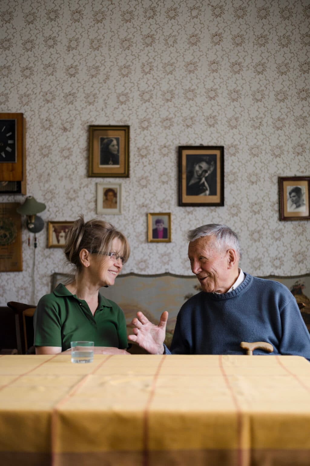 A younger woman shows a tablet to an older woman as they sit together, both smiling warmly. - Home Instead