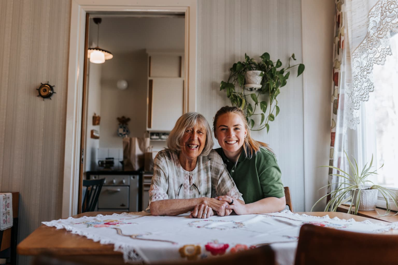A younger woman shows a tablet to an older woman as they sit together, both smiling warmly. - Home Instead